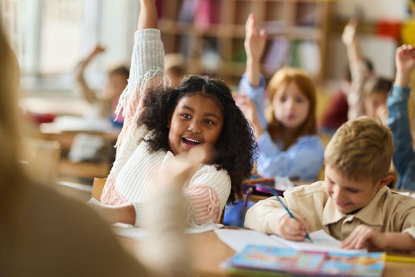 Estudiantes sonrientes levantan la mano en clase