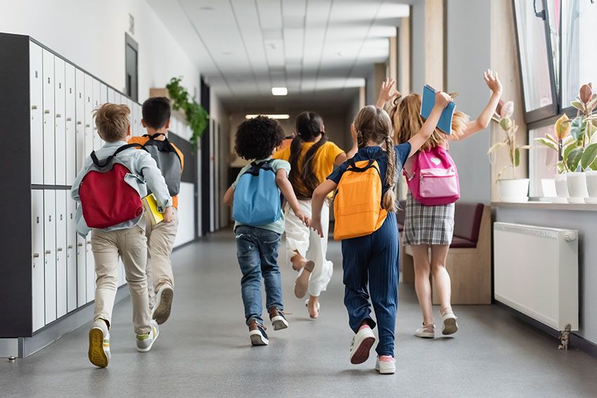 Niños corren con sus mochilas por el pasillo del colegio